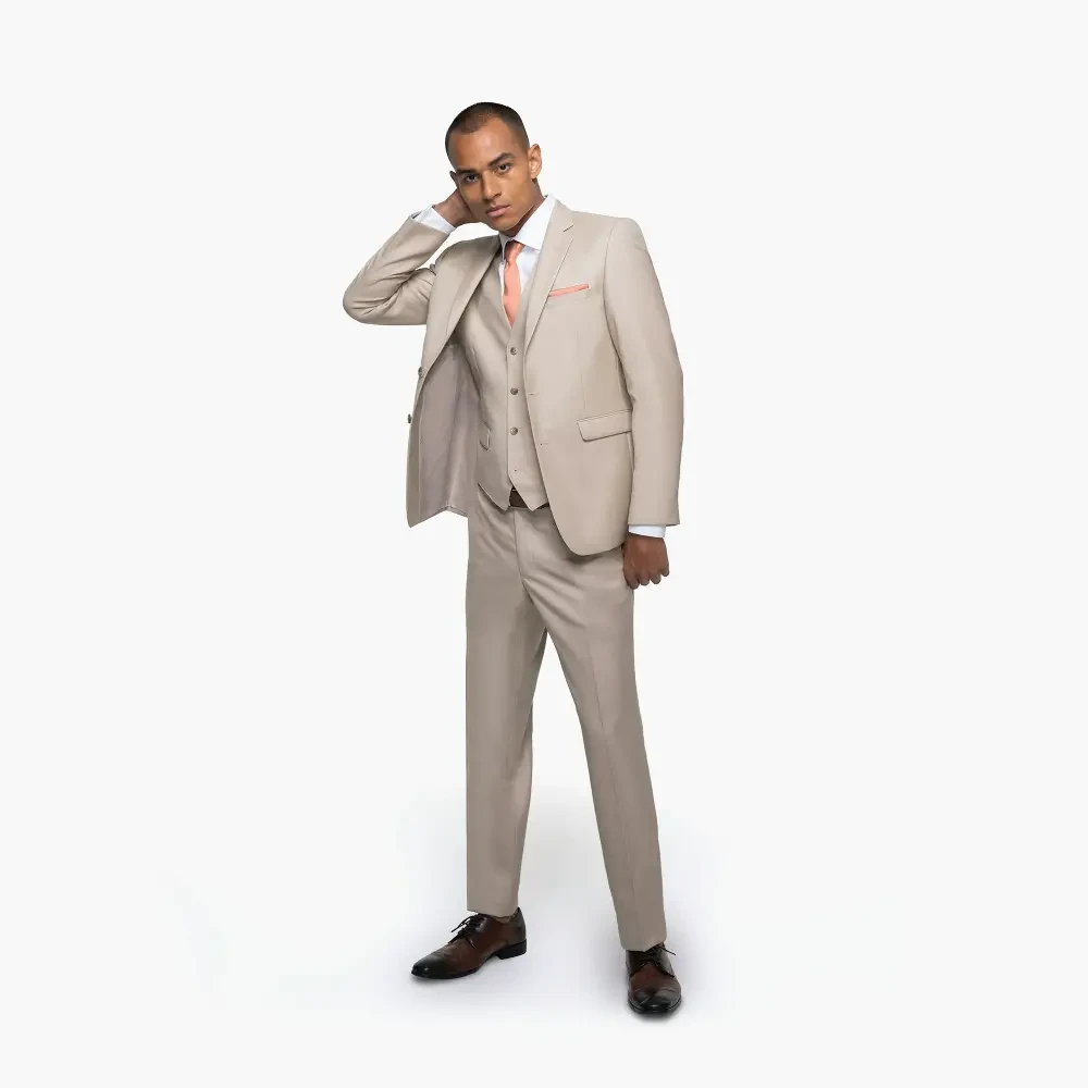 A man in a light beige suit with a vest, standing with one hand on his neck and a subtle smile.
