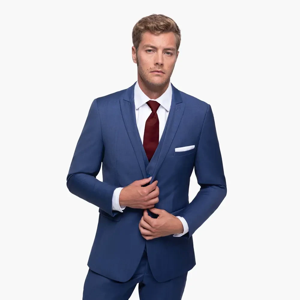 A man in a blue suit with a white shirt and a burgundy tie, posing confidently.