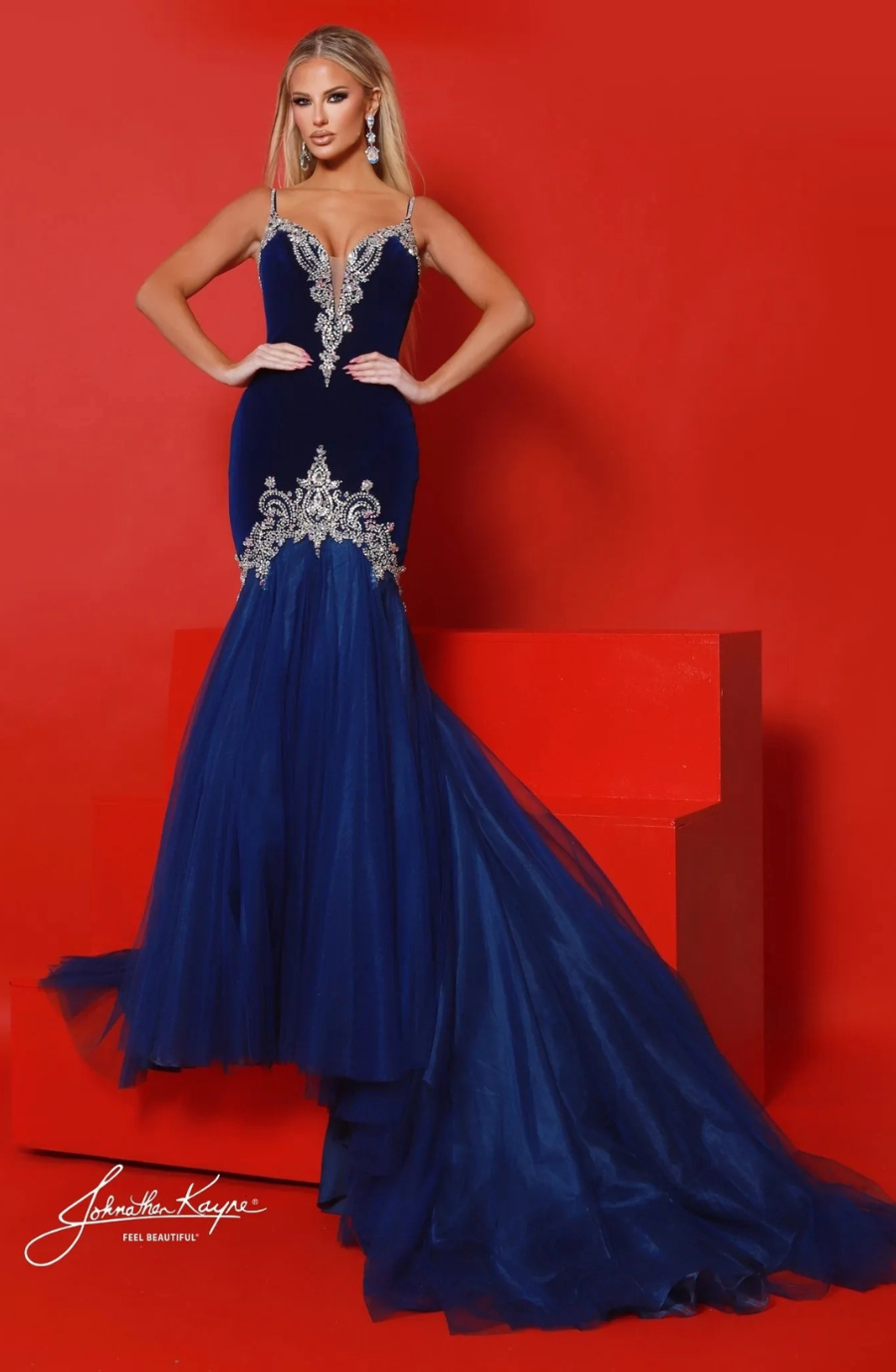 A woman wearing a blue evening gown with intricate silver embellishments, posing against a red background.