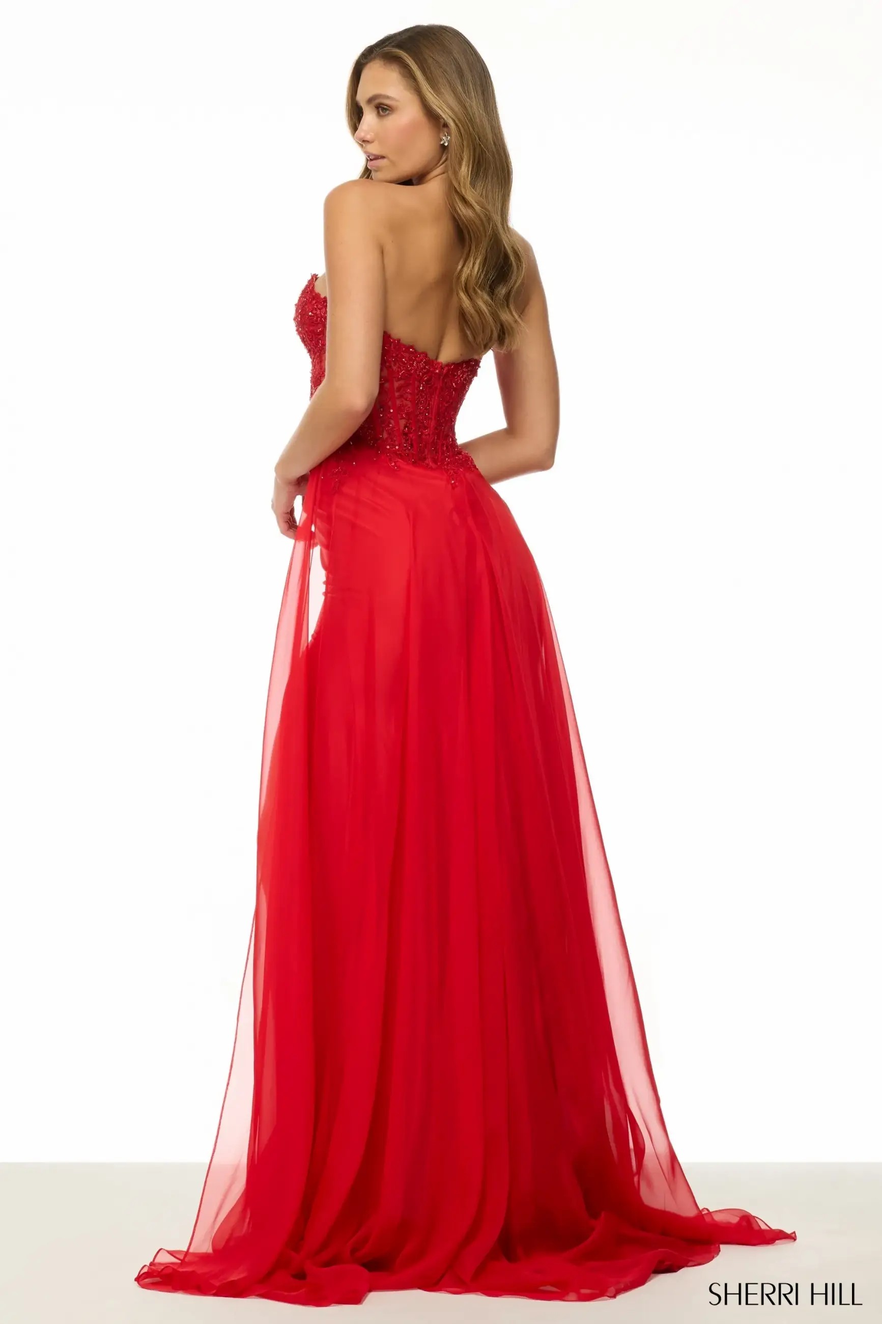 Model is wearing a red strapless chiffon fitted dress with a high slit