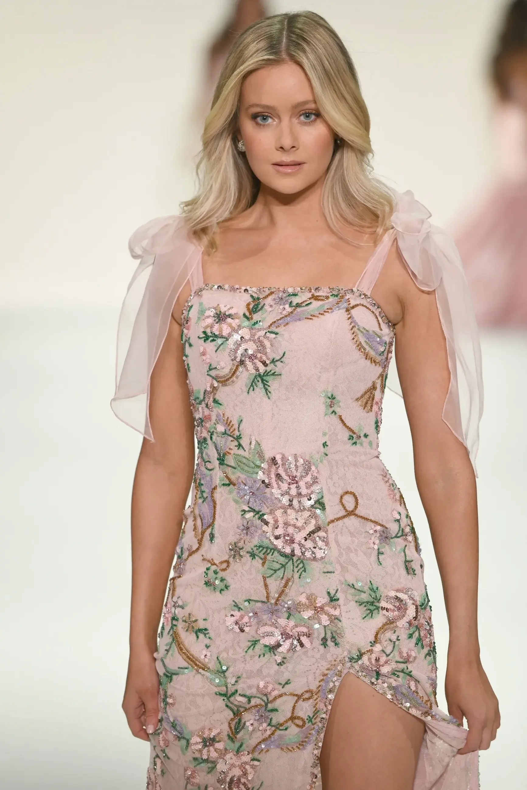 A model walks down the runway wearing a pink floral dress with sheer sleeves.