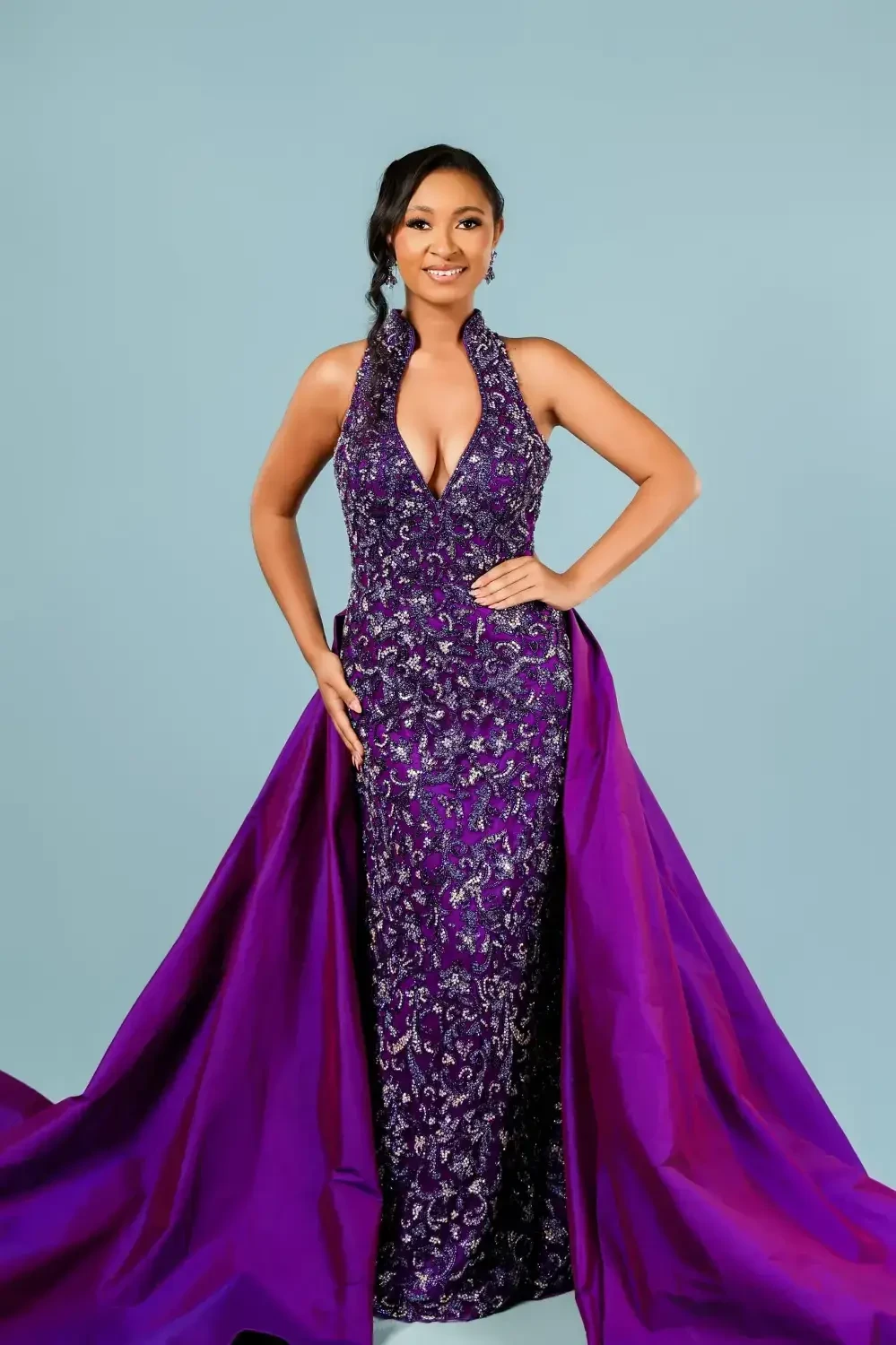 model is wearing a purple pageant dress with an overskirt