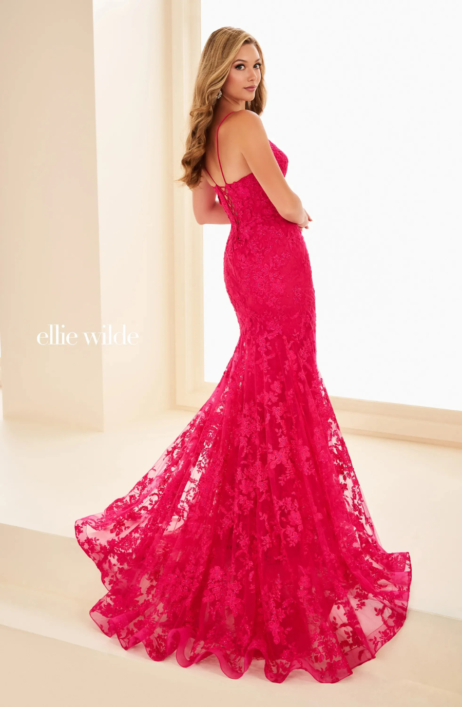 A woman in a fitted, bright pink lace gown with a mermaid silhouette, posing gracefully from the back.