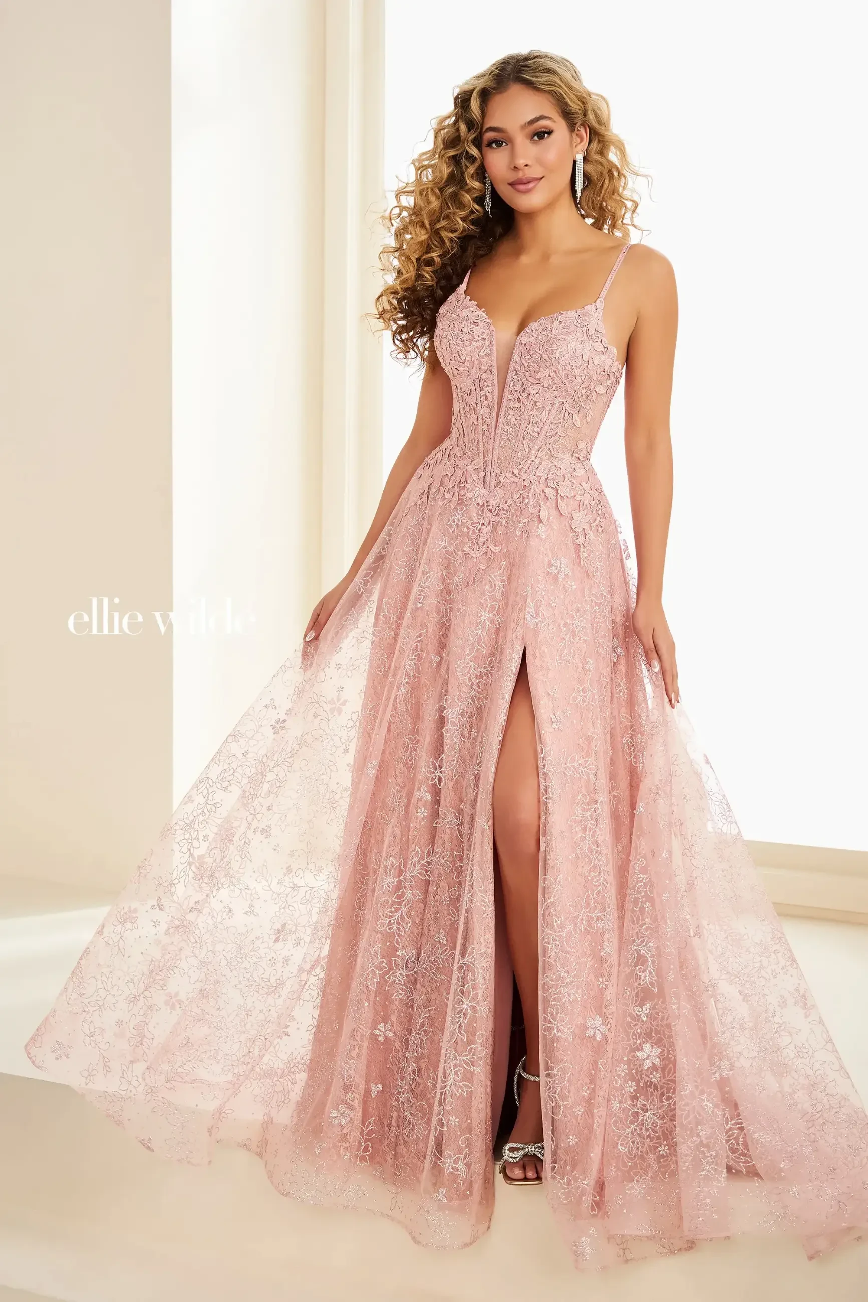 A woman in a pink lace evening gown with a deep neckline and thigh-high slit stands gracefully, exuding elegance and confidence.