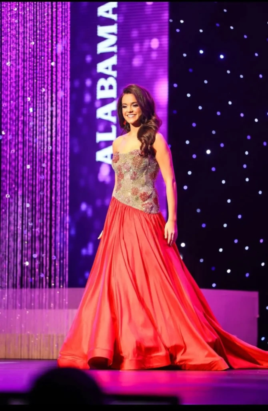 model is wearing a strapless coral colored pageant gown