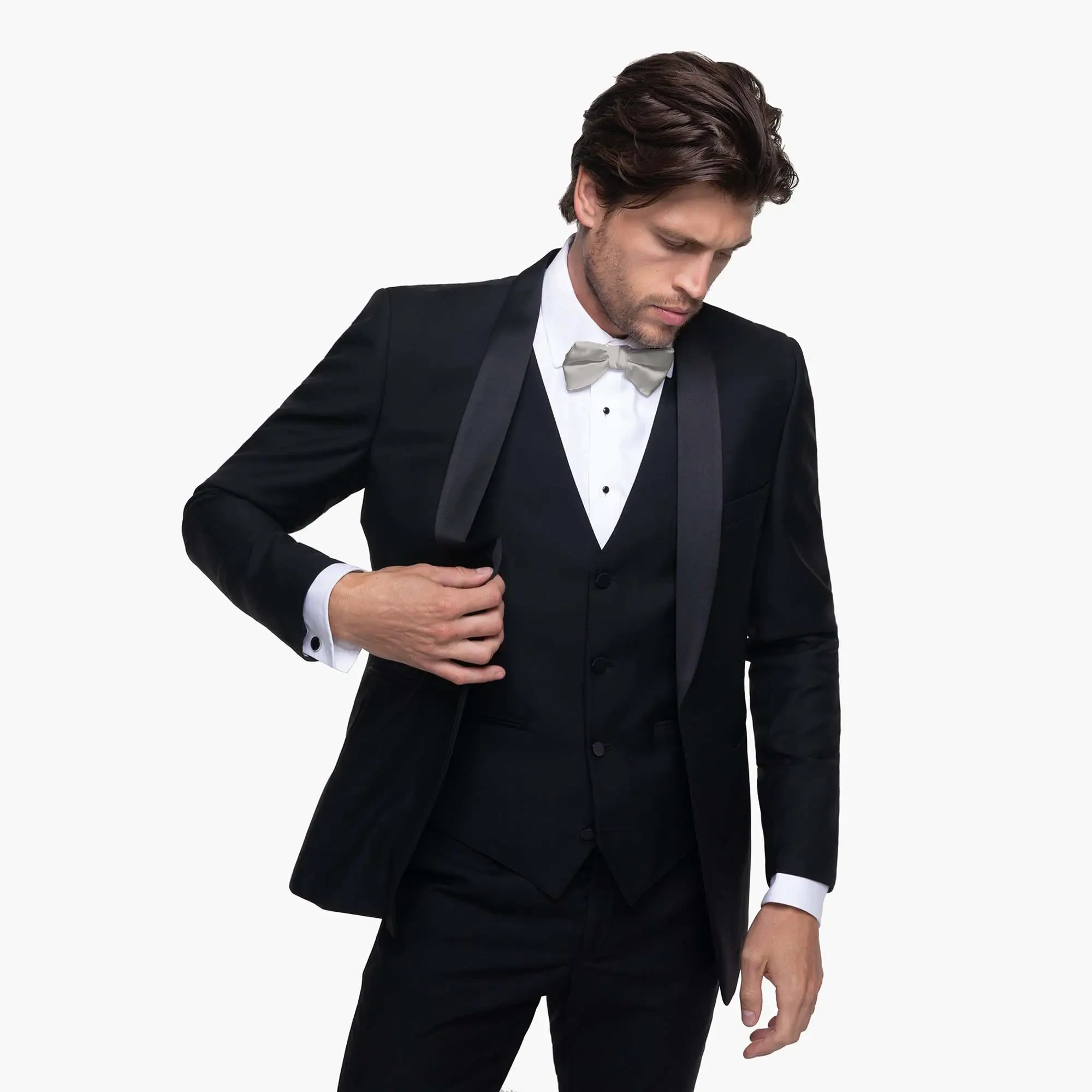 A man wearing a classic black tuxedo with a white shirt and silver bow tie adjusts his jacket. The mood is elegant and sophisticated.